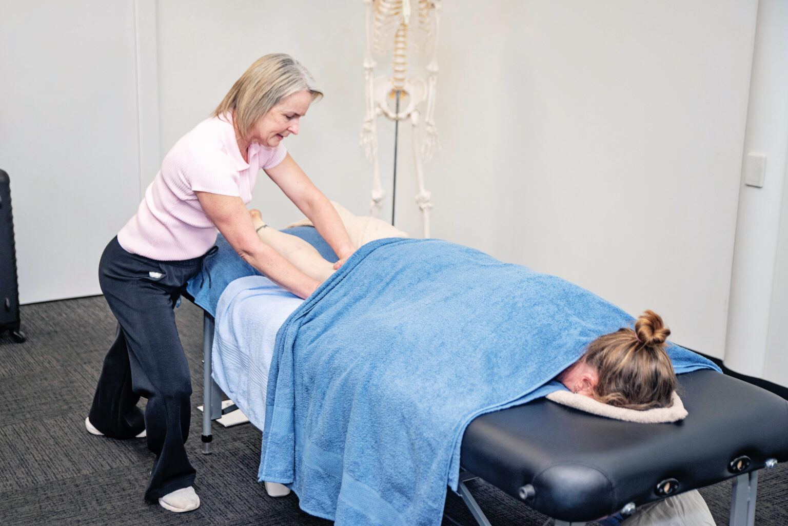 Linda Kenny demonstrating a hands-on massage technique on a client lying face down under a blue towel
