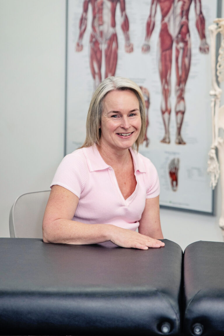 Linda Kenny seated at a treatment table in the teaching room, smiling